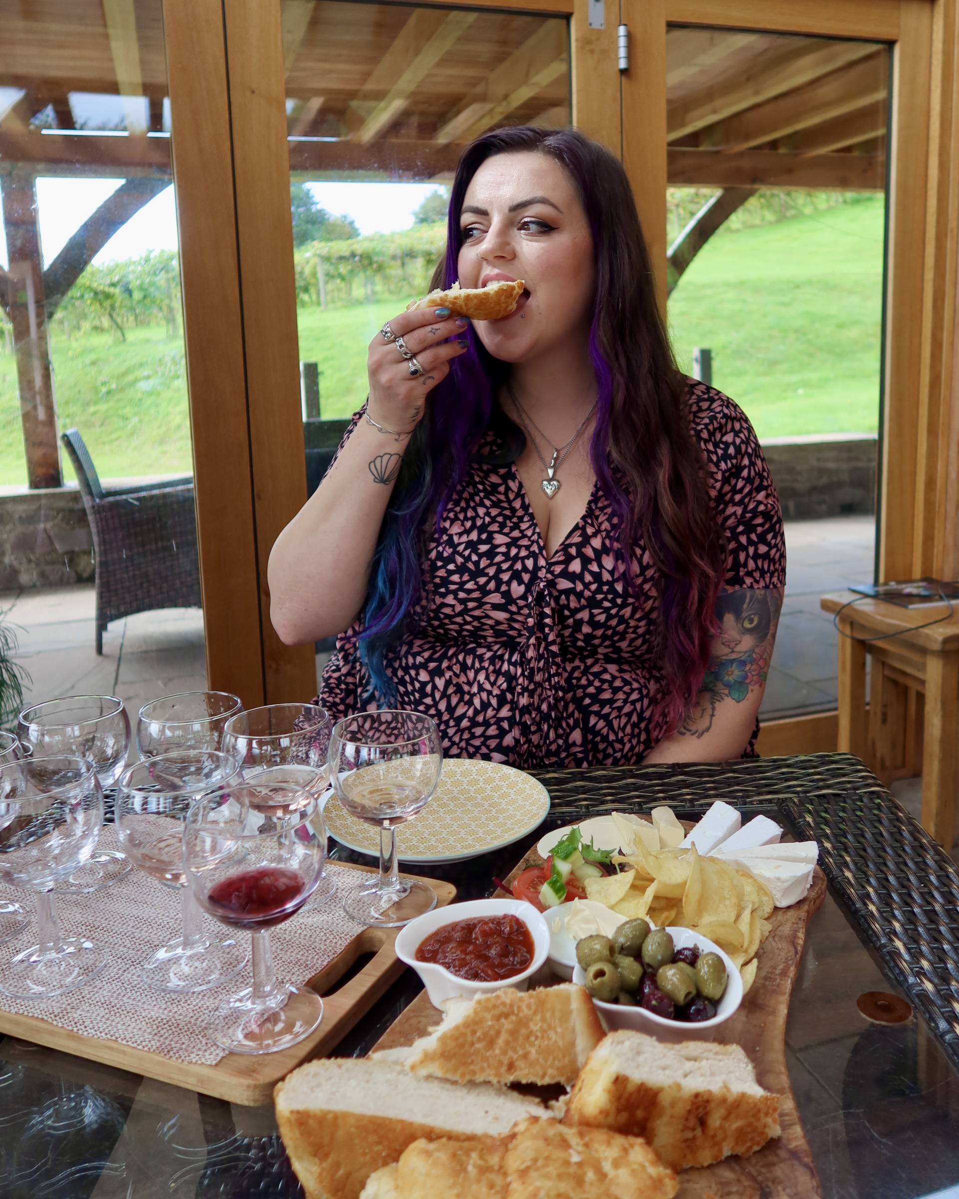 Luisa eats a piece of bread with a vegan cheese platter and wine tasting board in front of her at Sugar Loaf Vineyard